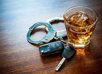 A glass of alcohol on a table beside a set of car keys and some handcuffs