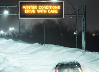 car driving in heavy snow an overhead freeway sign reads winter conditions drive with care